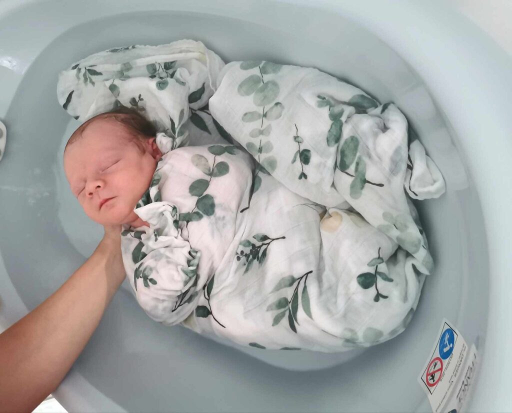 Nouveau-né emmailloté dans un lange fleuri, plongé dans l'eau du bain